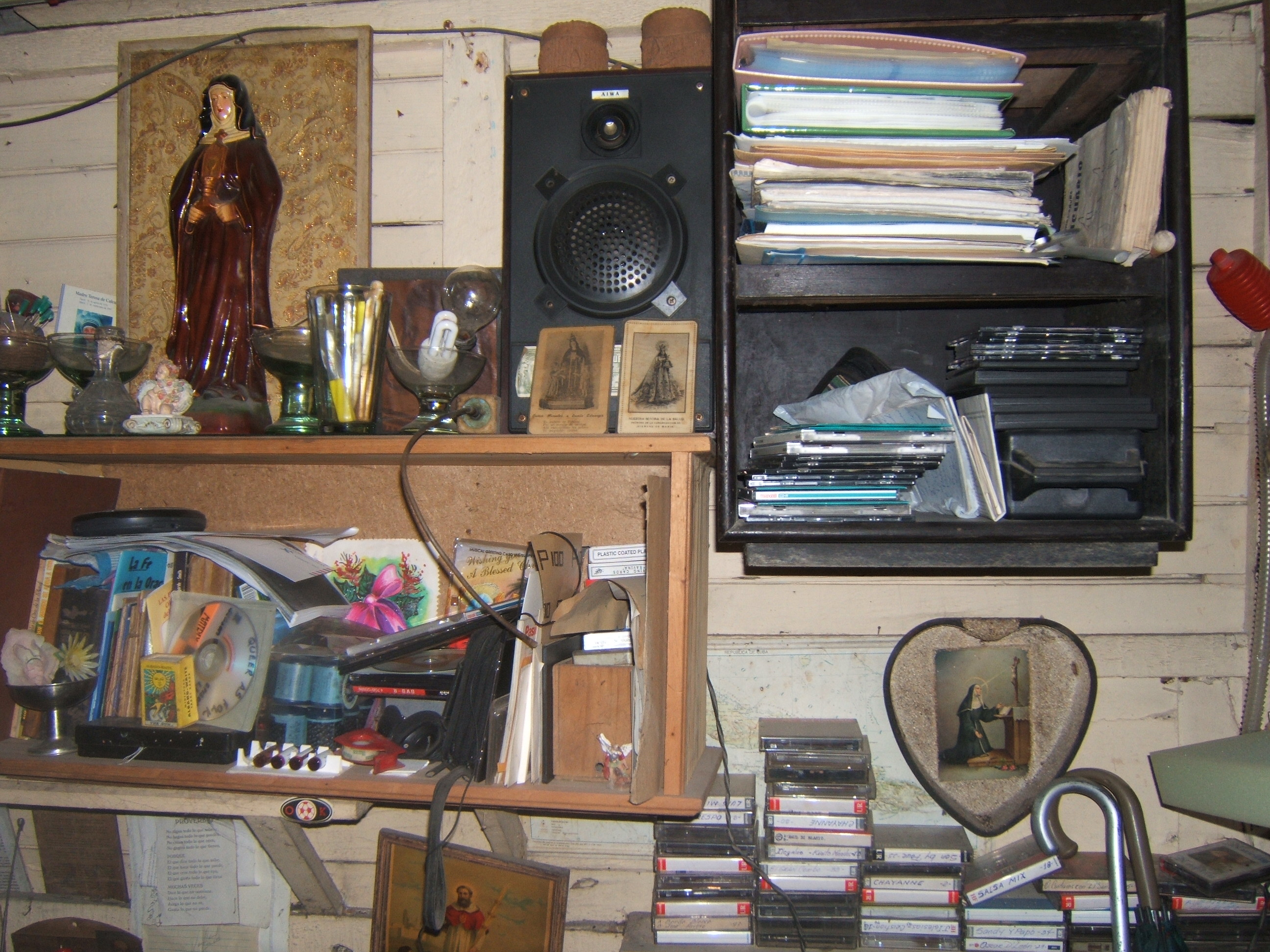 Figure 11. Another part of Pedro’s altar, showing a Santa Rita plaster figurine on a shelf, with other saints’ images, surrounded by cassettes, compact discs, notebooks, religious manuals, a speaker, and other supplies. Santiago de Cuba, August 2008. Photograph by author.