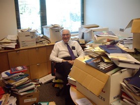 Jan Blommaert in a crowded office full of overflowing boxes of books.